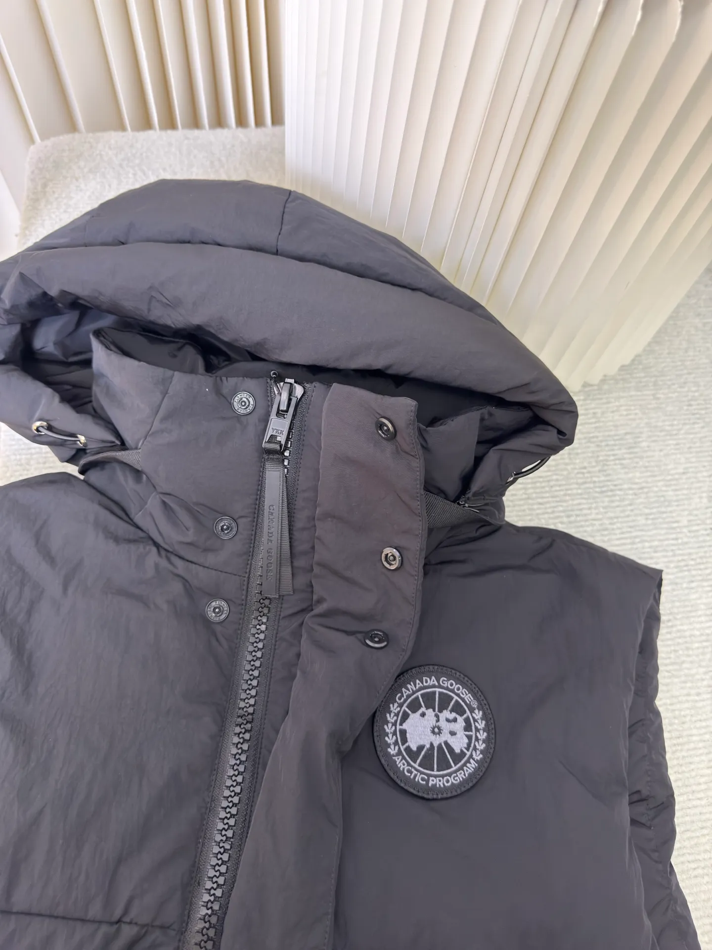 P760 Big Goose Logo Hooded Down Vest is made of high-quality protective nylon fabric, which not only enhances the wear resistance of the surface, but also takes into account wind resistance, ensuring excellent performance in various harsh weather conditions.  90 national standard high-quality white duck down: selected high-loft down, weighing 170g, light and warm, with excellent temperature locking performance and good resilience.  Three-dimensional quilting process: Precision thread reinforcement to prevent velvet drilling and ensure that the fluffy and resilient elasticity lasts as new.  Details: The ribbon is woven with polyester as the base. The brand letters are decorated on the ribbon through high-precision computer embroidery. The edges of the pattern are clear, the stitches are fine and even, and multiple layers of embroidery thread are stacked to enhance the three-dimensional effect. Size S M L XL